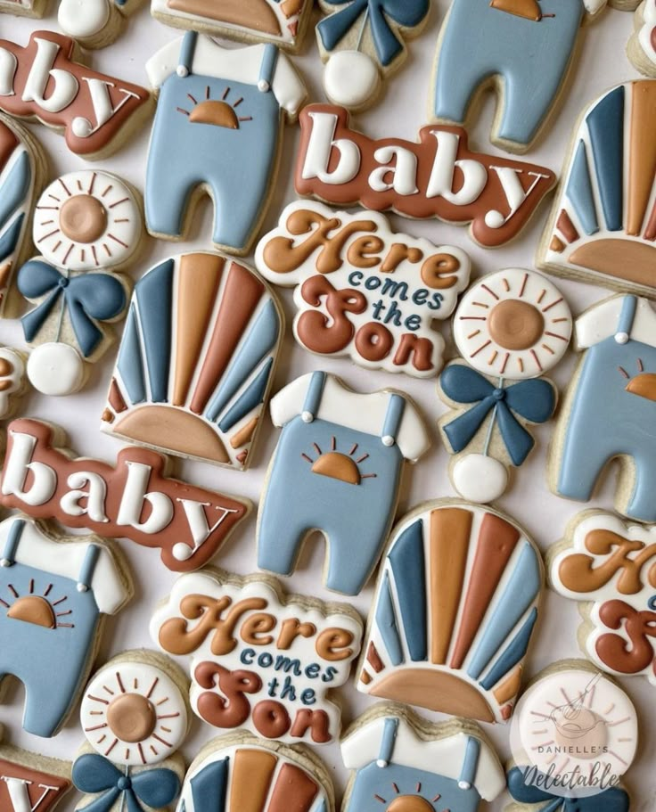 baby shower cookies are arranged in rows on a white tablecloth with blue, orange and brown designs