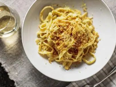 a white bowl filled with pasta on top of a table next to a glass of wine