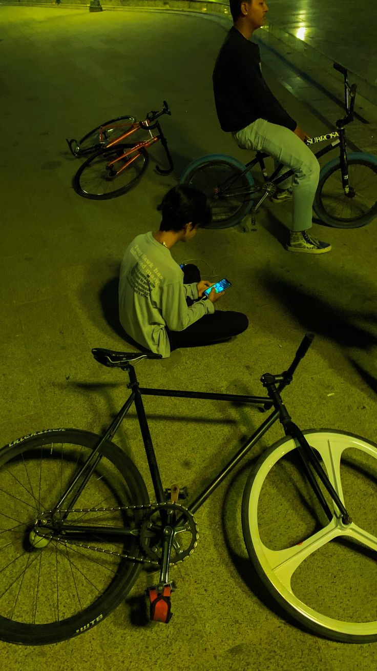 a man sitting on the ground next to a bike and looking at his cell phone