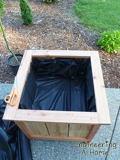 a wooden box sitting on top of a sidewalk next to a trash bag and scissors