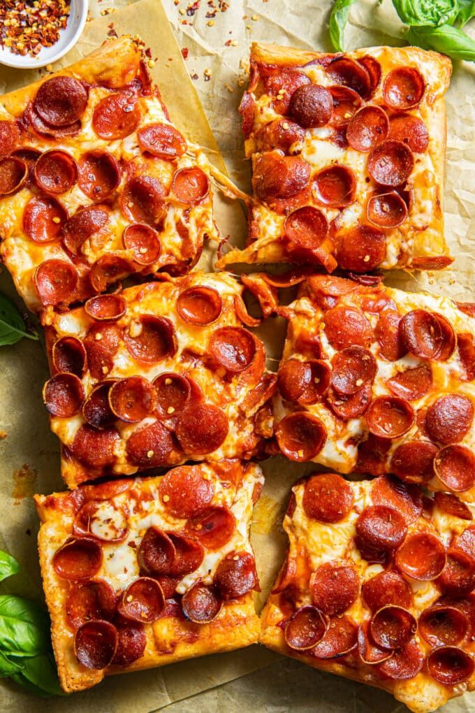 pepperoni pizza cut into squares on top of a wooden cutting board with basil leaves