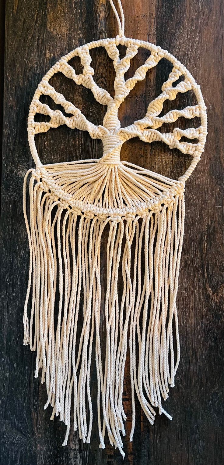 a white macrame hanging on a wooden wall with a tree in the middle