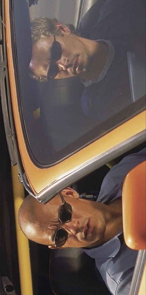 a man sitting in the driver's seat of a yellow vehicle looking at his reflection