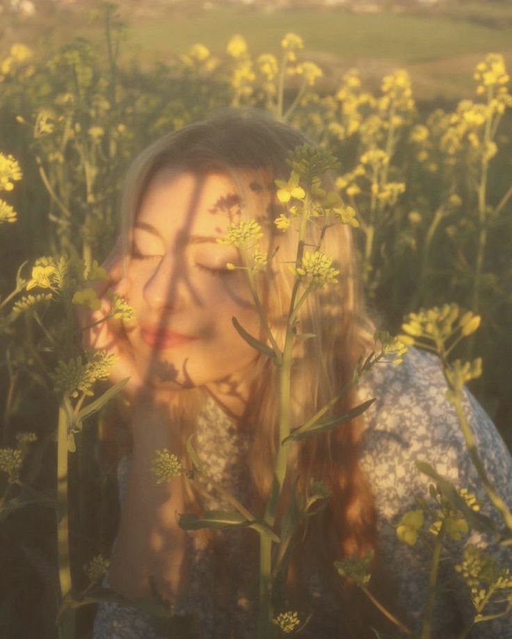 a woman is standing in a field with yellow flowers and looking up at the camera