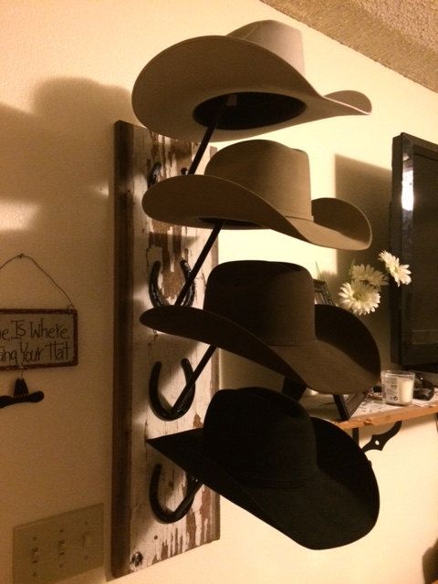 several hats are hanging on a wall near a mirror and coat rack with flowers in it