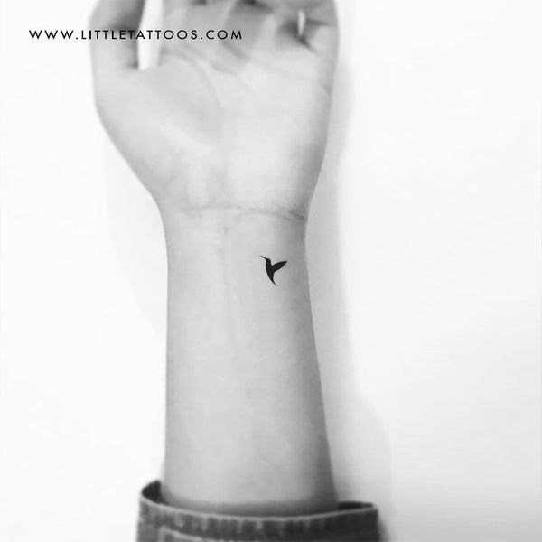 a small black bird tattoo on the left wrist, with an arrow in the middle