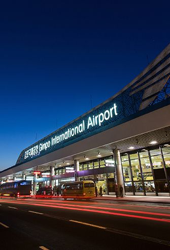 an airport terminal at night time with cars passing by on the road and in front of it