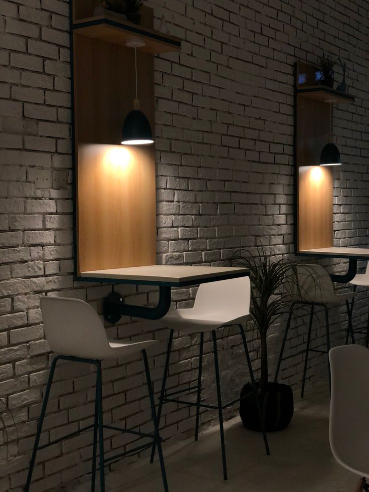 three white chairs are sitting in front of a brick wall with two lights on it