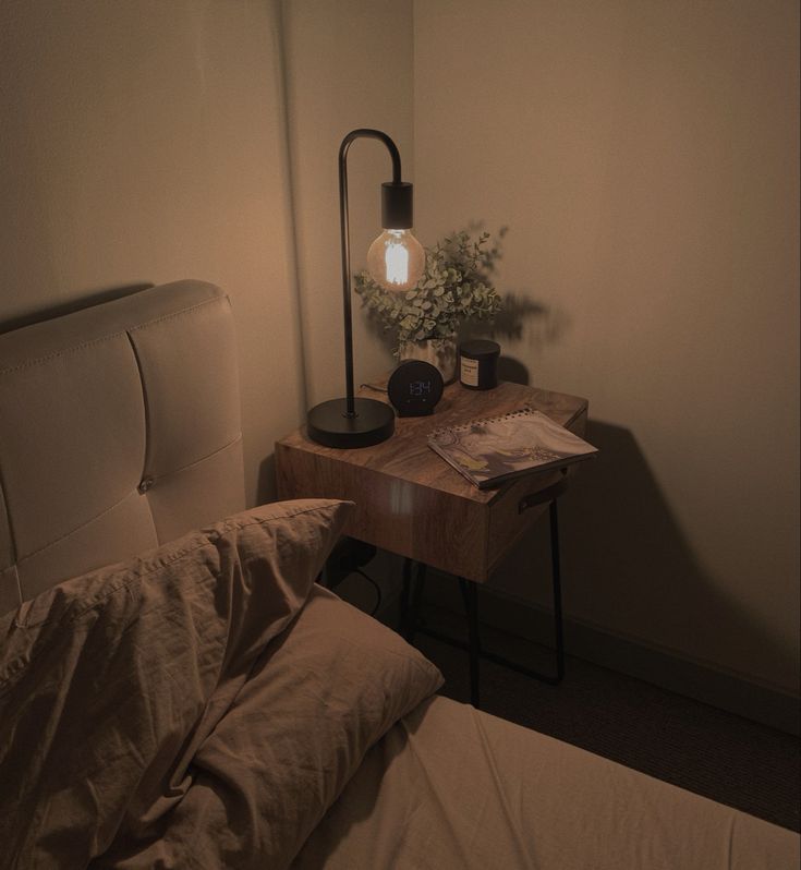 a small table with a lamp on it next to a bed