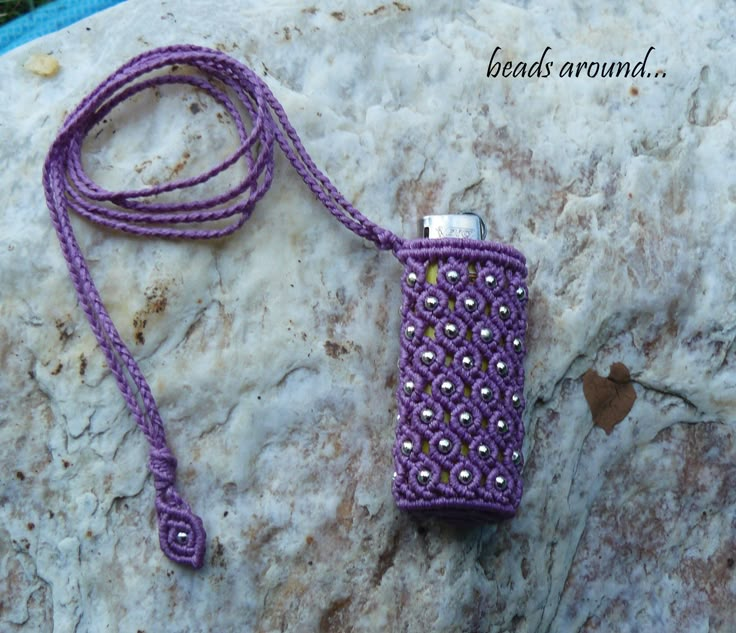 a purple crocheted cell phone case sitting on top of a rock with beads around it