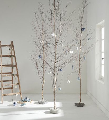 three small trees with ornaments on them in front of a ladder, window and wall