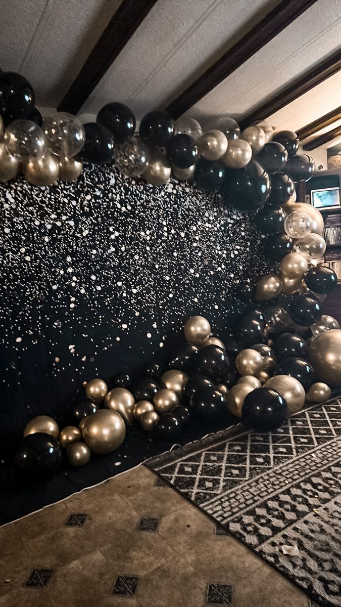 black and gold balloons are on the floor in front of a wall with an area rug