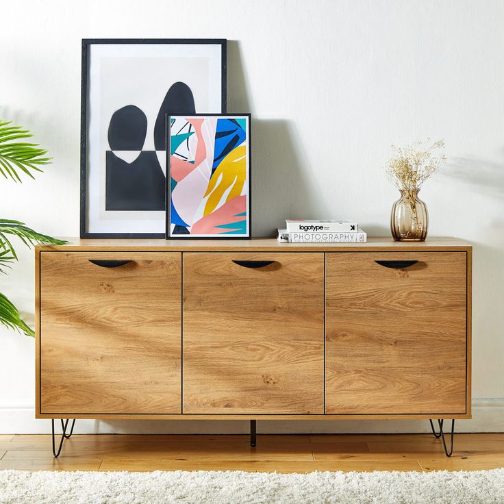 a wooden sideboard with two drawers and some pictures on it next to a potted plant