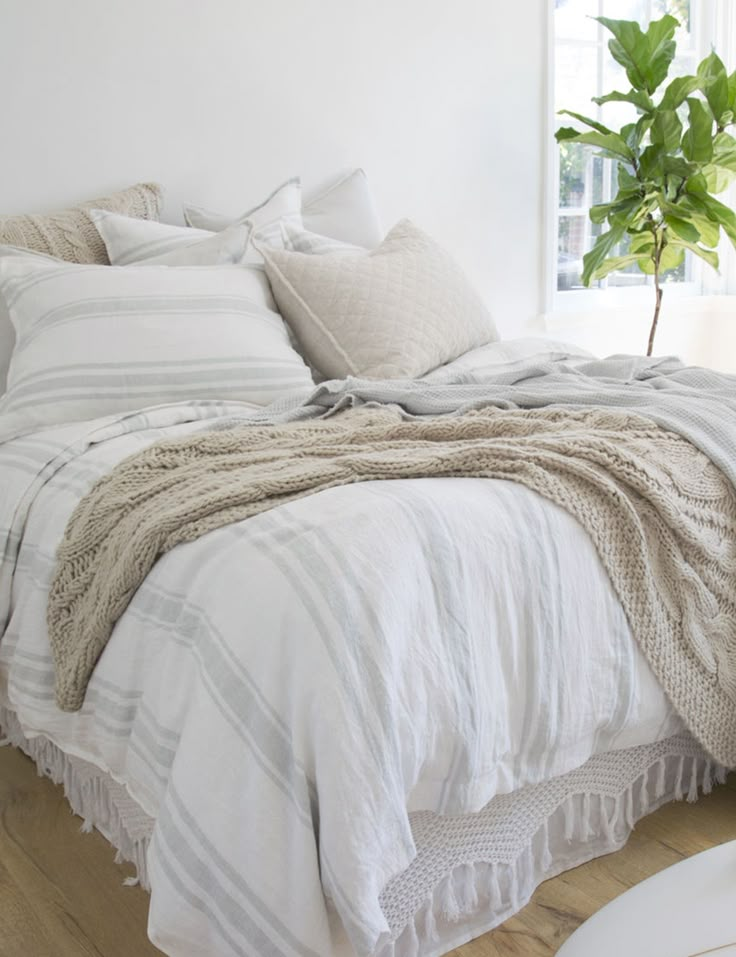 a bed with white linens and pillows in a room next to a potted plant