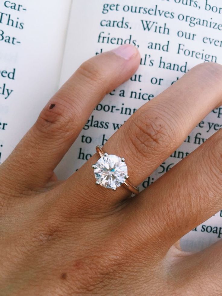 a person's hand with a ring on it and an open book in the background