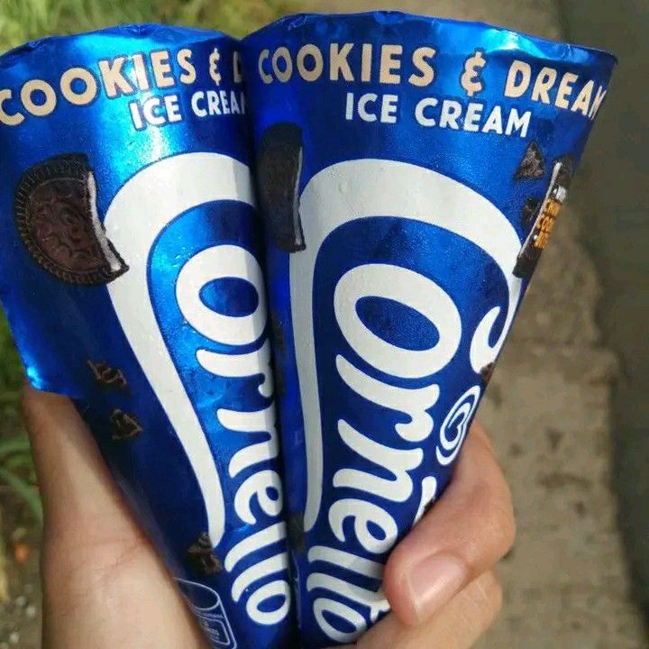 two cookies and cream ice cream cones are held in their hands, one is blue