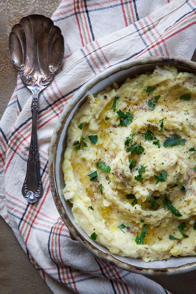 a bowl of mashed potatoes with meat and parsley on the side next to two spoons