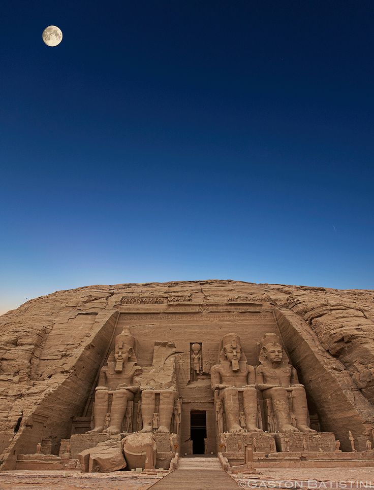 the entrance to an ancient egyptian temple under a blue sky with a full moon in the distance