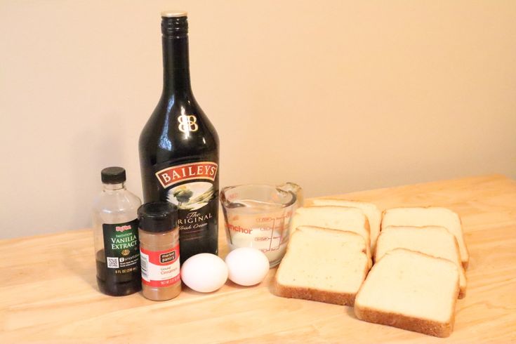 the ingredients to make an egg sandwich are displayed on a wooden table with a bottle of booze