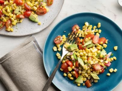 two plates with corn, tomatoes and avocado on them next to a fork