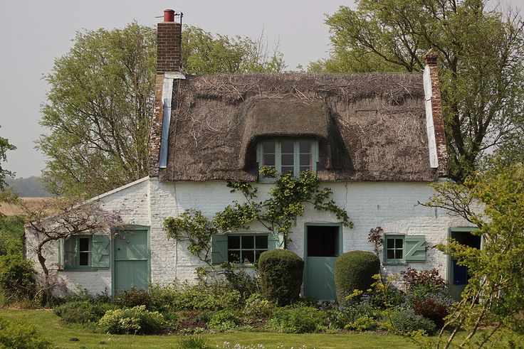 an old white house with a thatched roof and green shutters on the windows