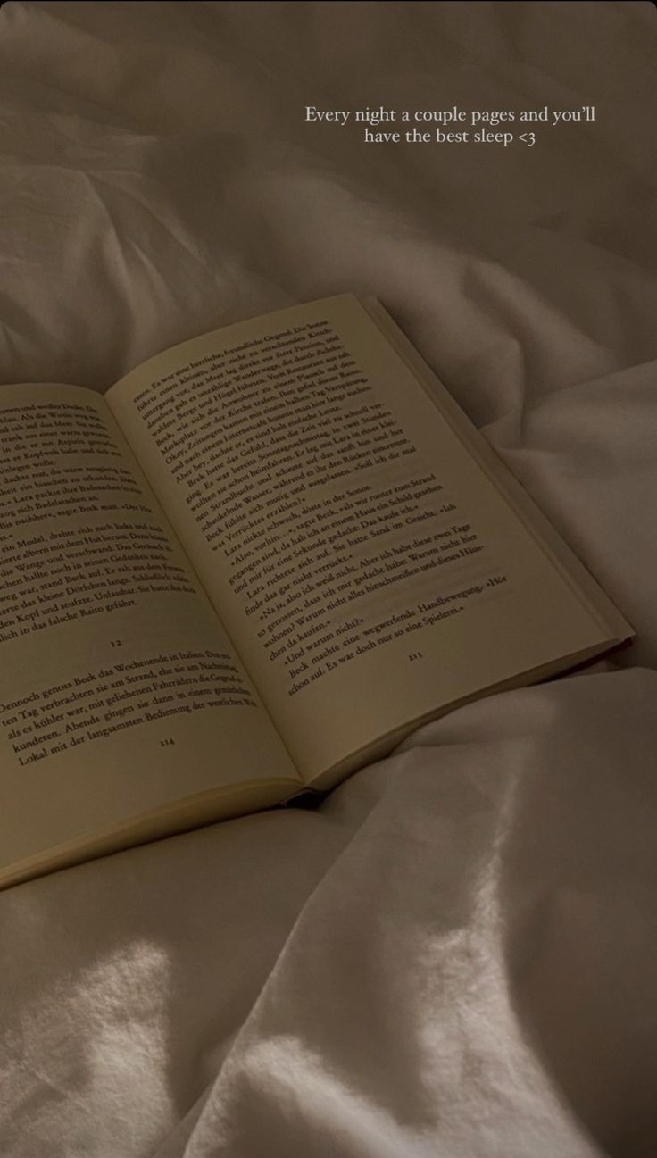 an open book sitting on top of a white sheet covered bed next to a pillow