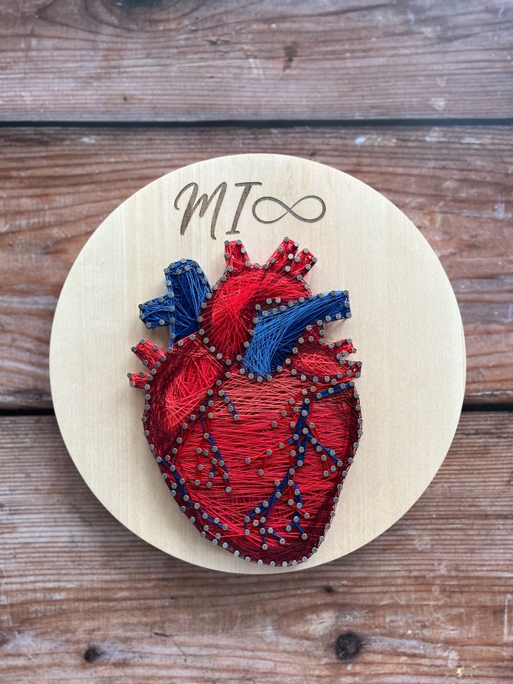 an embroidered heart on a wooden plate with the word mtta written in it and beads