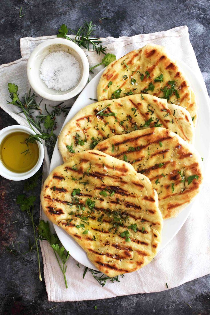 grilled flatbreads on a plate next to dipping sauce and sprig of parsley