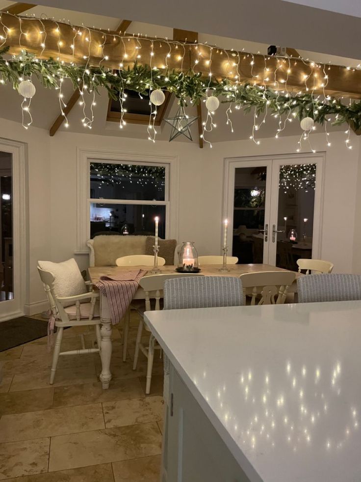 a kitchen filled with lots of white furniture and christmas lights hanging from the ceiling above it