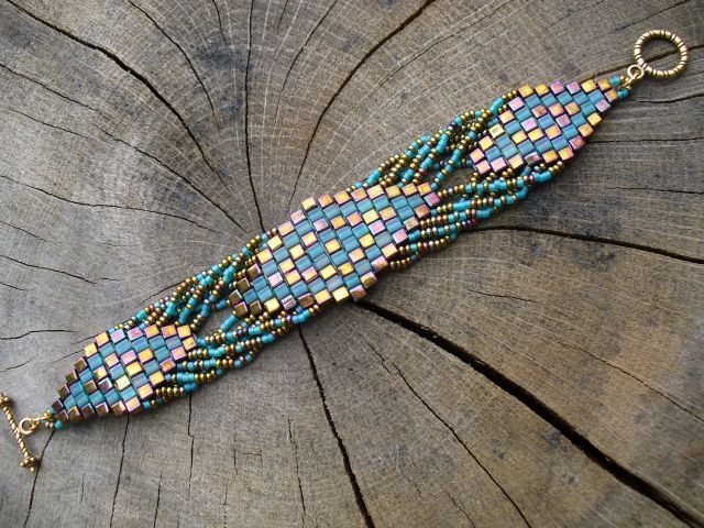 a beaded bracelet sitting on top of a piece of wood with chains hanging from it