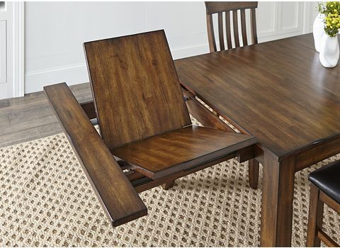 a wooden table with two chairs and a vase on top of it, in front of a white wall