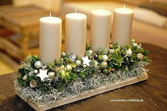 four white candles are sitting on a table with greenery and ornaments around them,