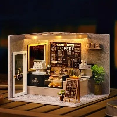 a miniature model of a coffee shop with lights on the windows and signs in front