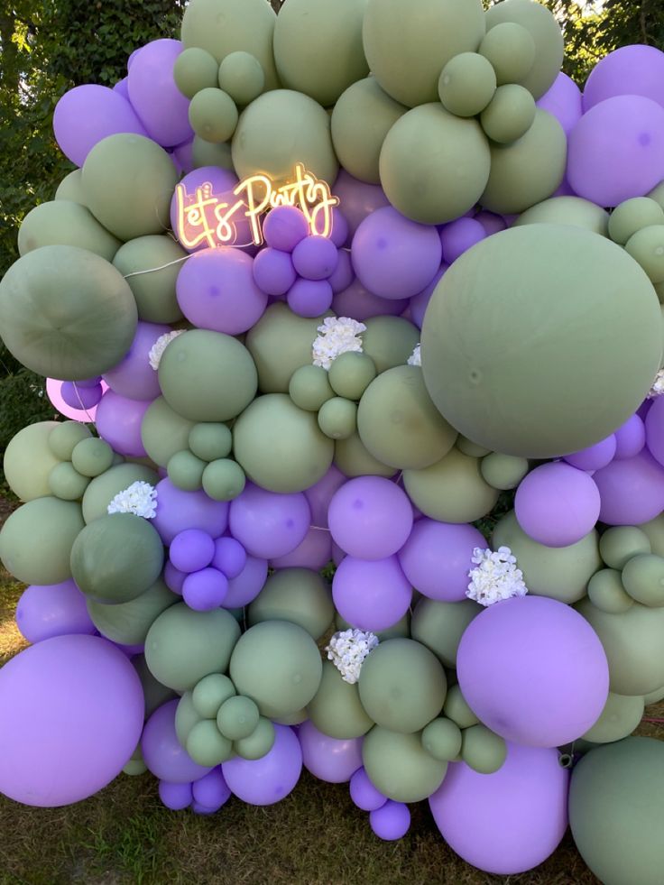 purple and green balloons are arranged in the shape of a tree with a neon sign that reads let's party