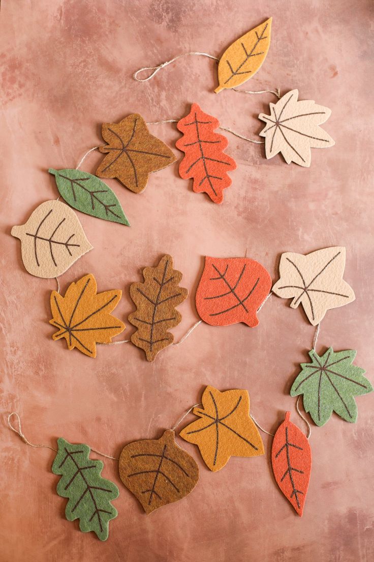 fall leaves and acorns are hung on a pink background with twine strings