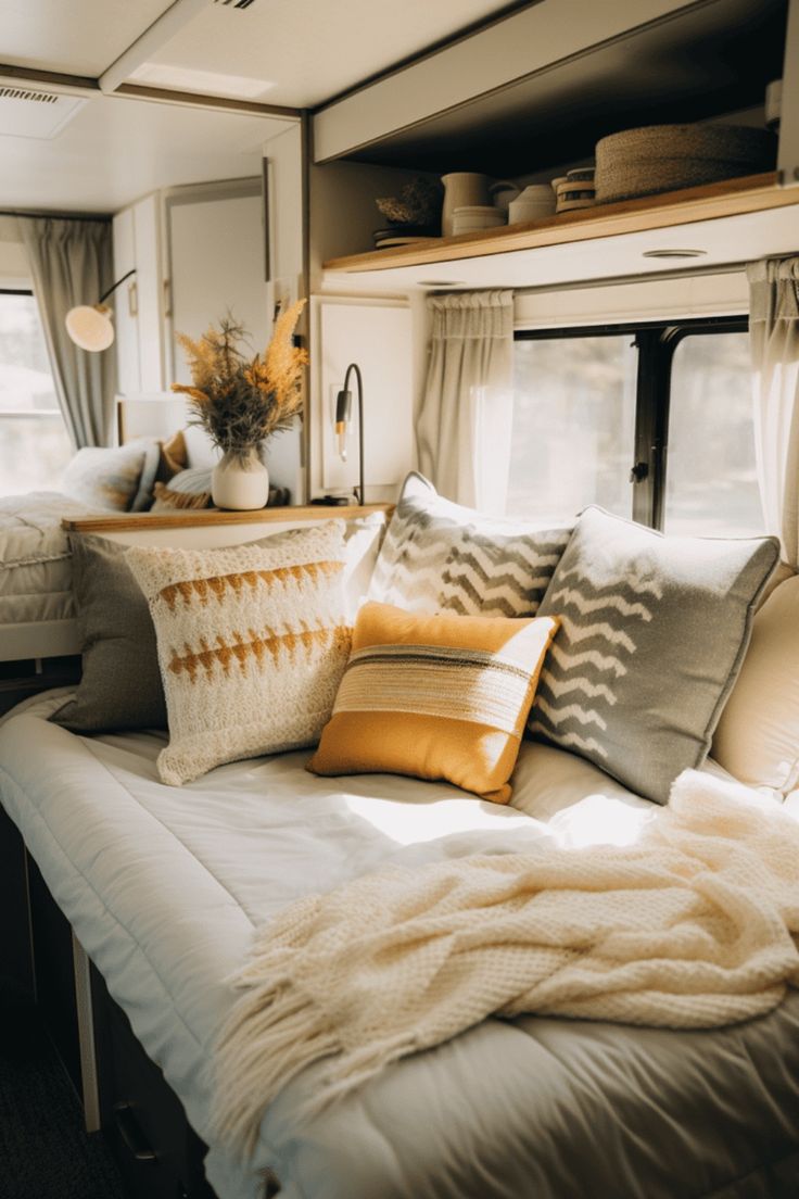 a bed with pillows and blankets on top of it in a room filled with windows