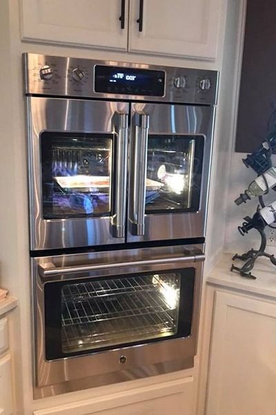 two ovens are built into the wall in this kitchen with white cabinets and stainless steel appliances