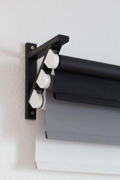 a close up of a curtain rod on a white wall with black and grey curtains