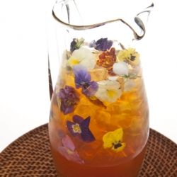 a pitcher filled with water and flowers on top of a brown tablecloth covered place mat