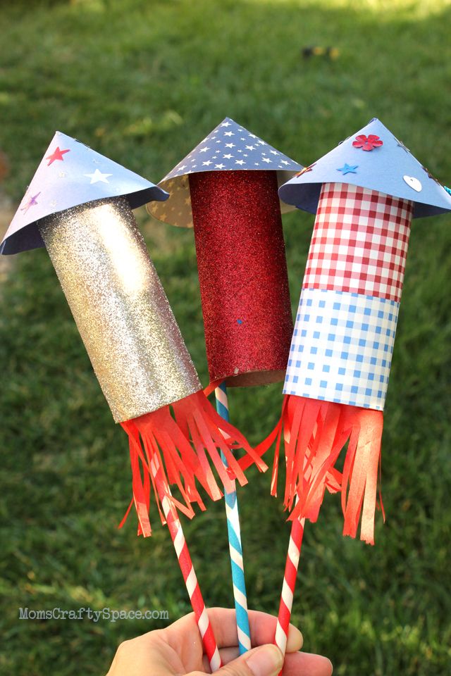 hand holding three paper straws with red, white and blue decorations on them in the grass