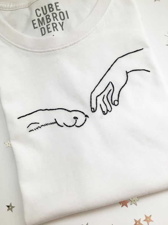 a white t - shirt with the creation of two hands touching each other's fingers