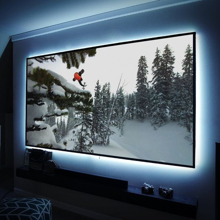 a large television mounted to the side of a wall in a living room with snow covered trees