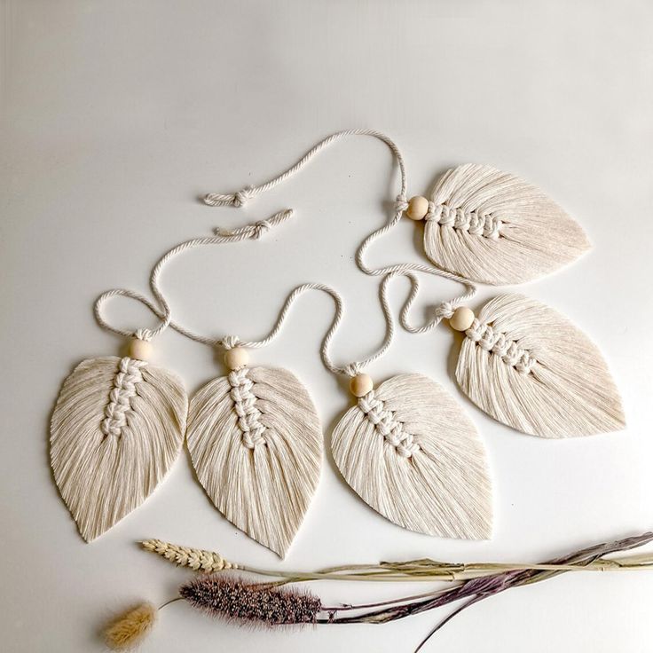 four white leaf shaped pendants are hanging on a string with some dried flowers nearby