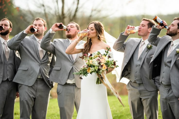 a bride and groom drinking from their wedding party's bottles while standing in the grass