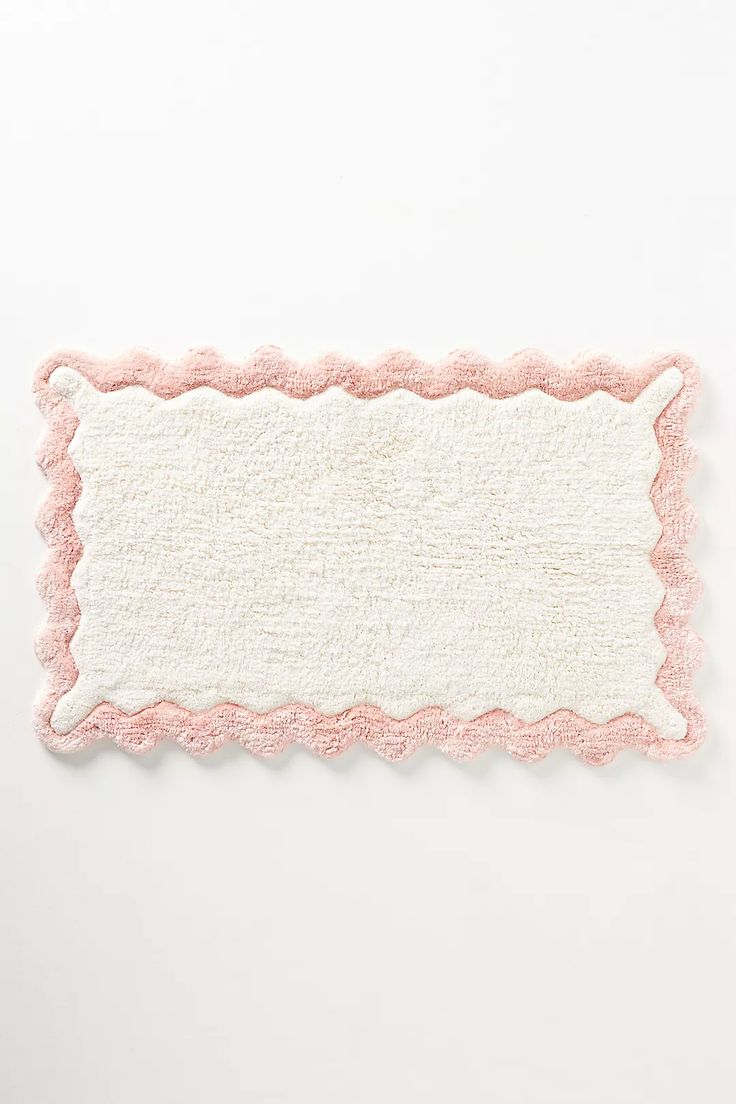 a pink and white rug with scalloped edges on a white surface, in the shape of a rectangle