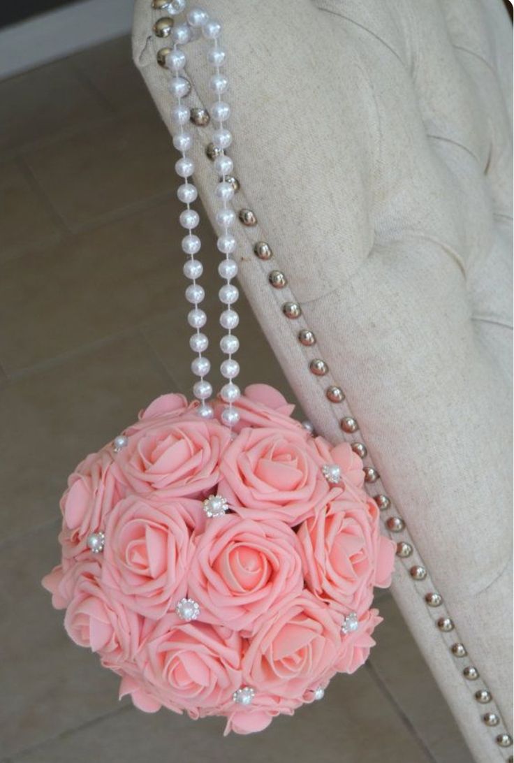 a bouquet of pink roses hanging from the back of a chair with pearls on it