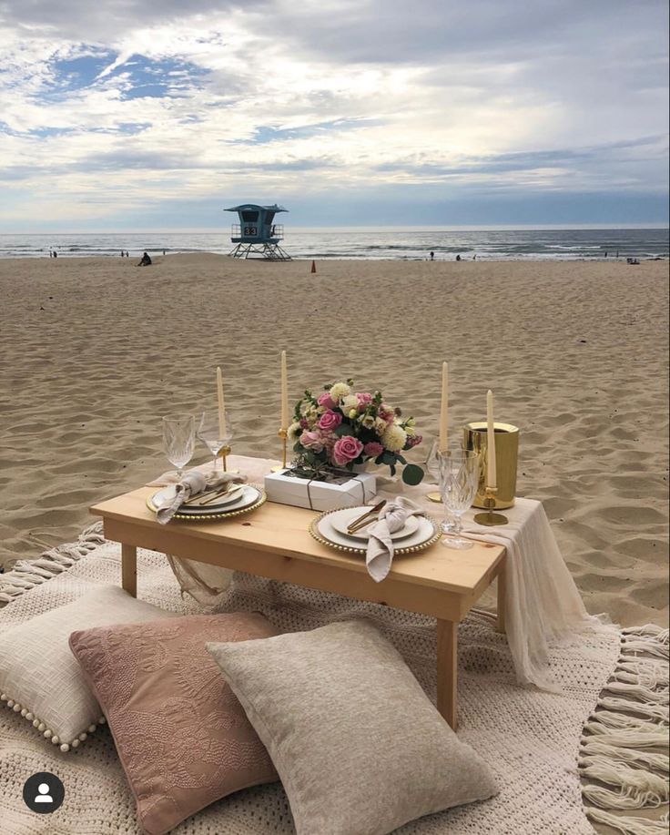 a table set for two on the beach with flowers and candles in front of it