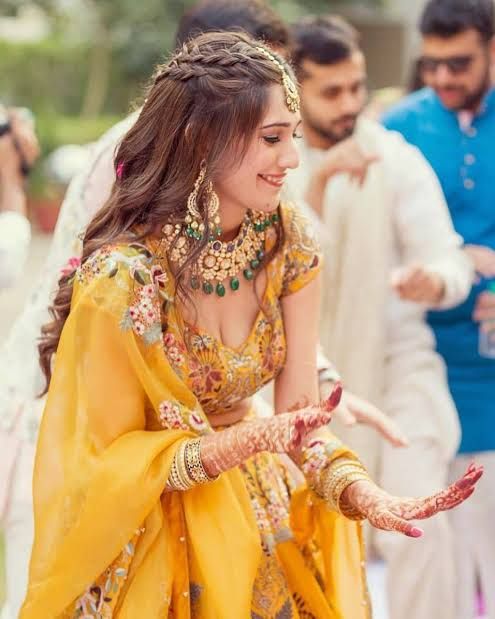 a woman in yellow and gold dress holding her hands out to the side with other people behind her