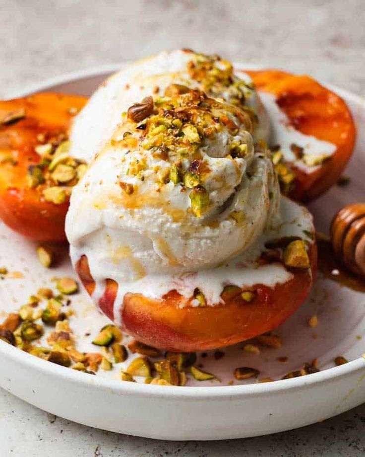 an ice cream sundae with peaches and pistachios on a white plate