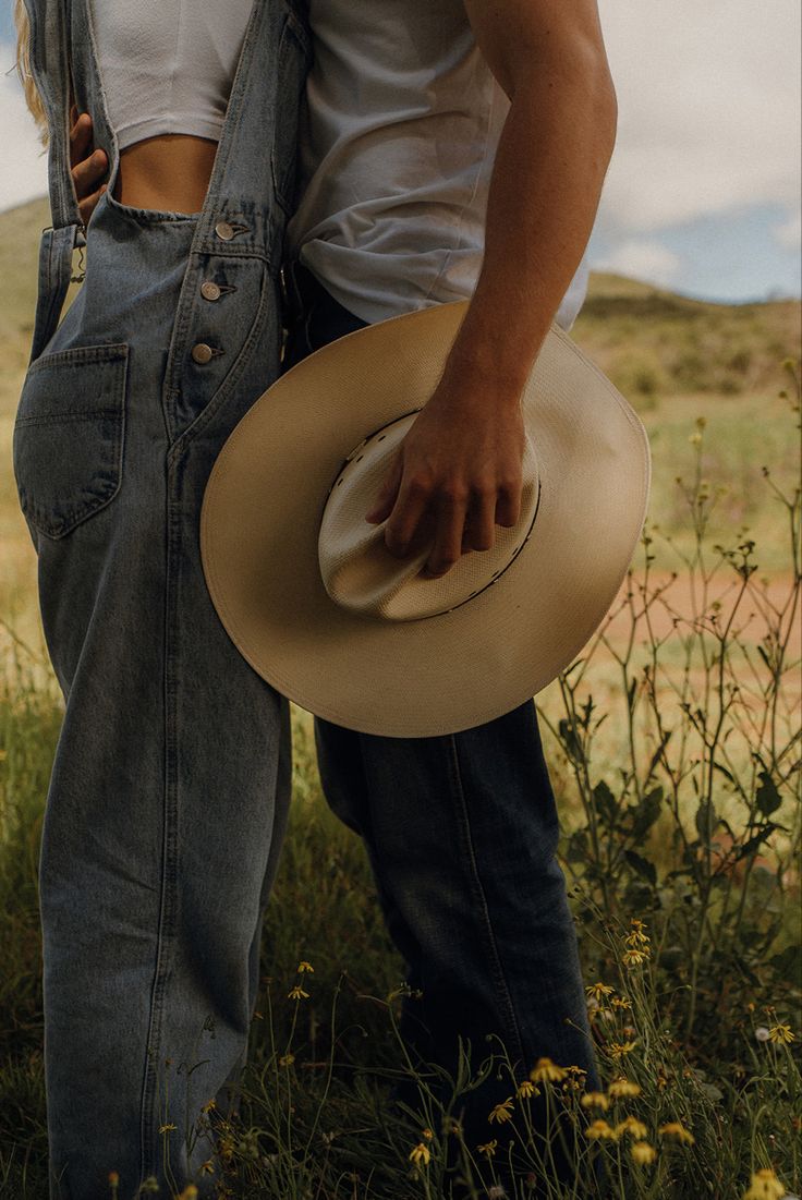 two people in overalls and cowboy hats standing next to each other with their arms around one another